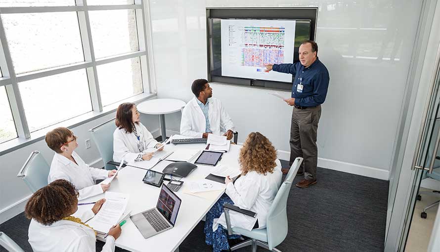 A group of researchers in a conference room look at a chart on a wall