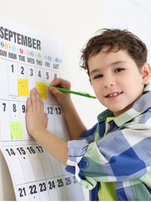 Young boy writing on a wall calendar to stay organized
