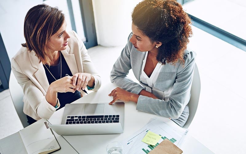 two women working together on a laptop in an office