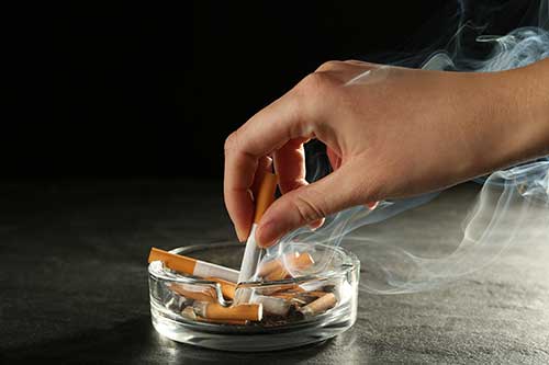 a hand extinguishing cigarette in glass ashtray