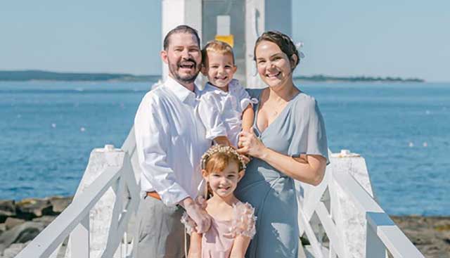 Husband with brain cancer, his wife, and their two young children posing at the beach for a family photo