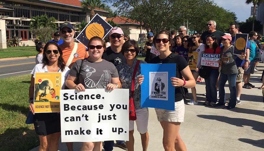 A group of researchers with signs promoting science. One says: Science. Because you can't just make it up.
