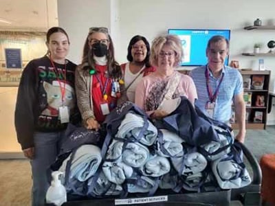 A group of five people stand behind a cart filled with rolled up blankets while smiling.