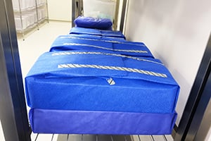 Boxes of surgical instruments wrapped in sterile blue surgical wraps sit on a shelf