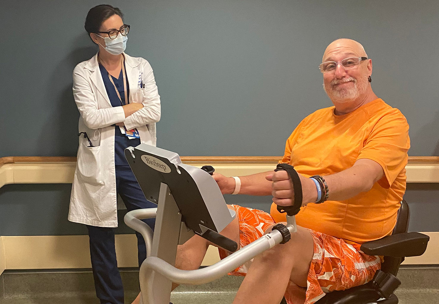 Dr. Freeman watches a patient use a semi-recumbent elliptical machine 