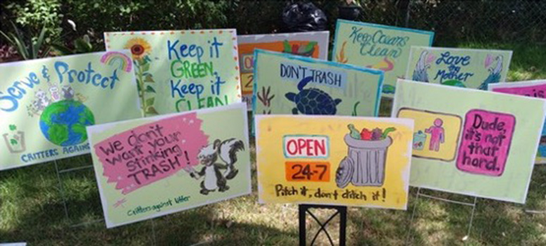 Multiple signs with painted messages are shown sticking out of the ground. The signs have conservation and anti-litter messages.
