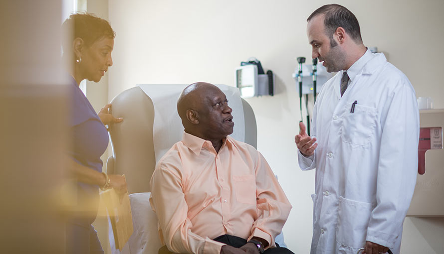 A doctor talks to a patient while his wife stands beside him
