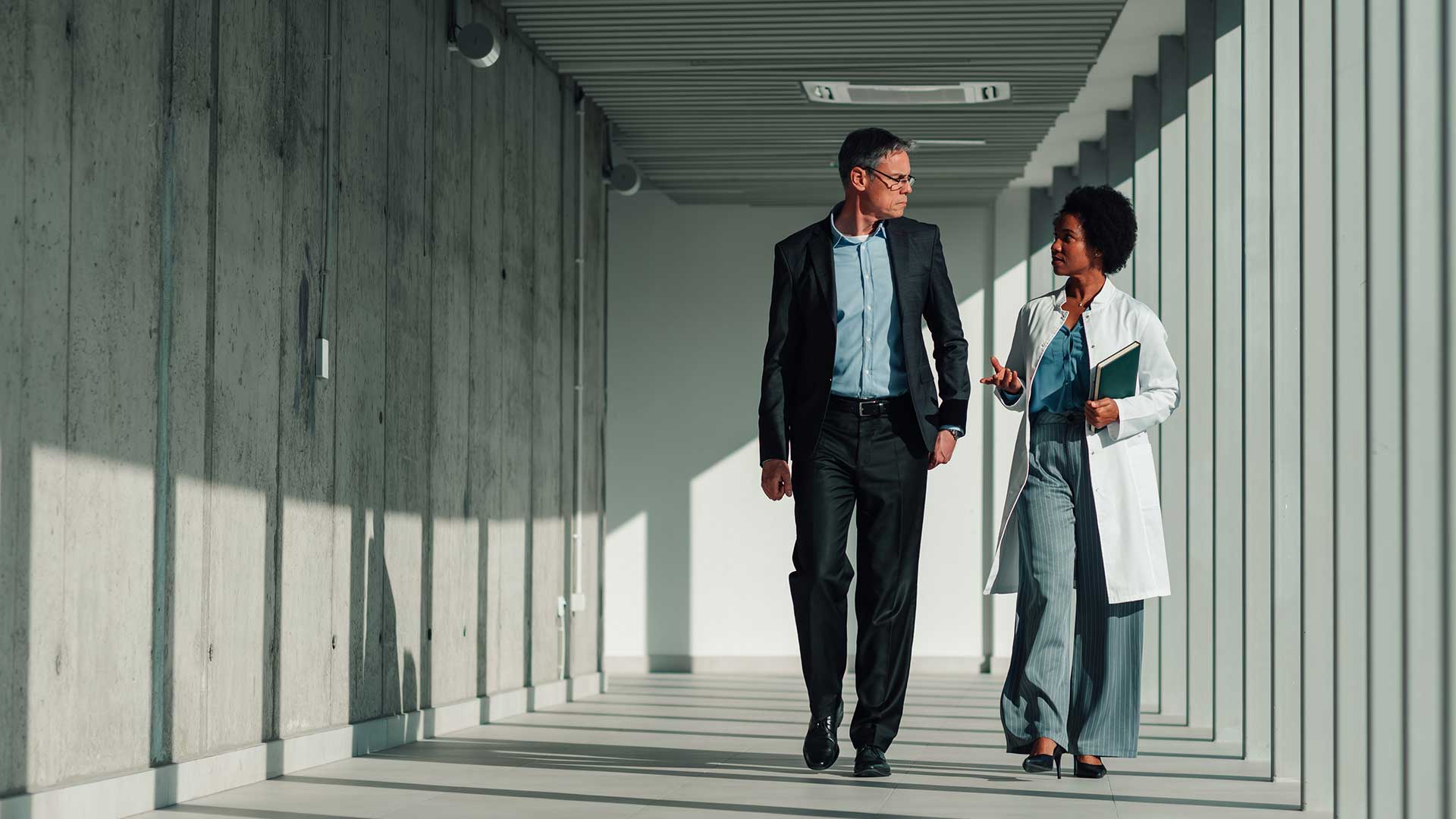 A man and a woman walk down a office building hallway.