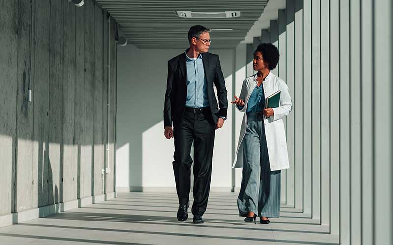 A man and a woman walk down a office building hallway.