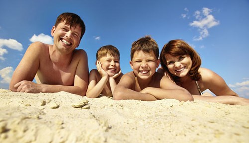 white family sitting on sand at a beach could be a Basal Cell Carcinoma Risk Factor