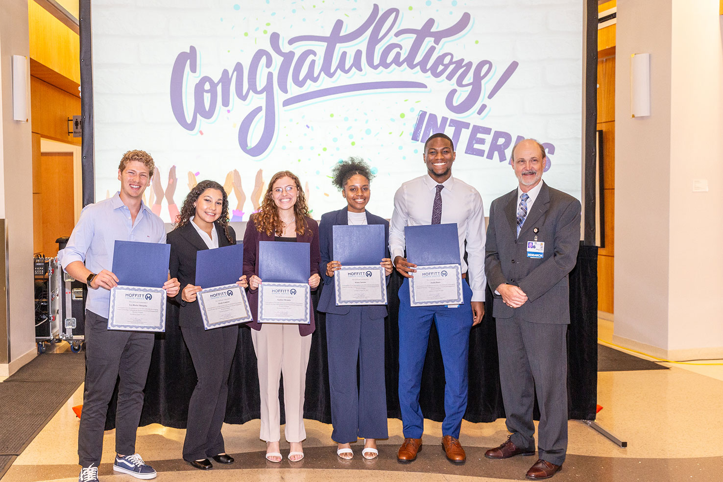 Interns celebrate in front of congratulations sign