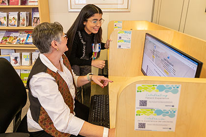 A patient uses one of the library computers with help from one of the staff