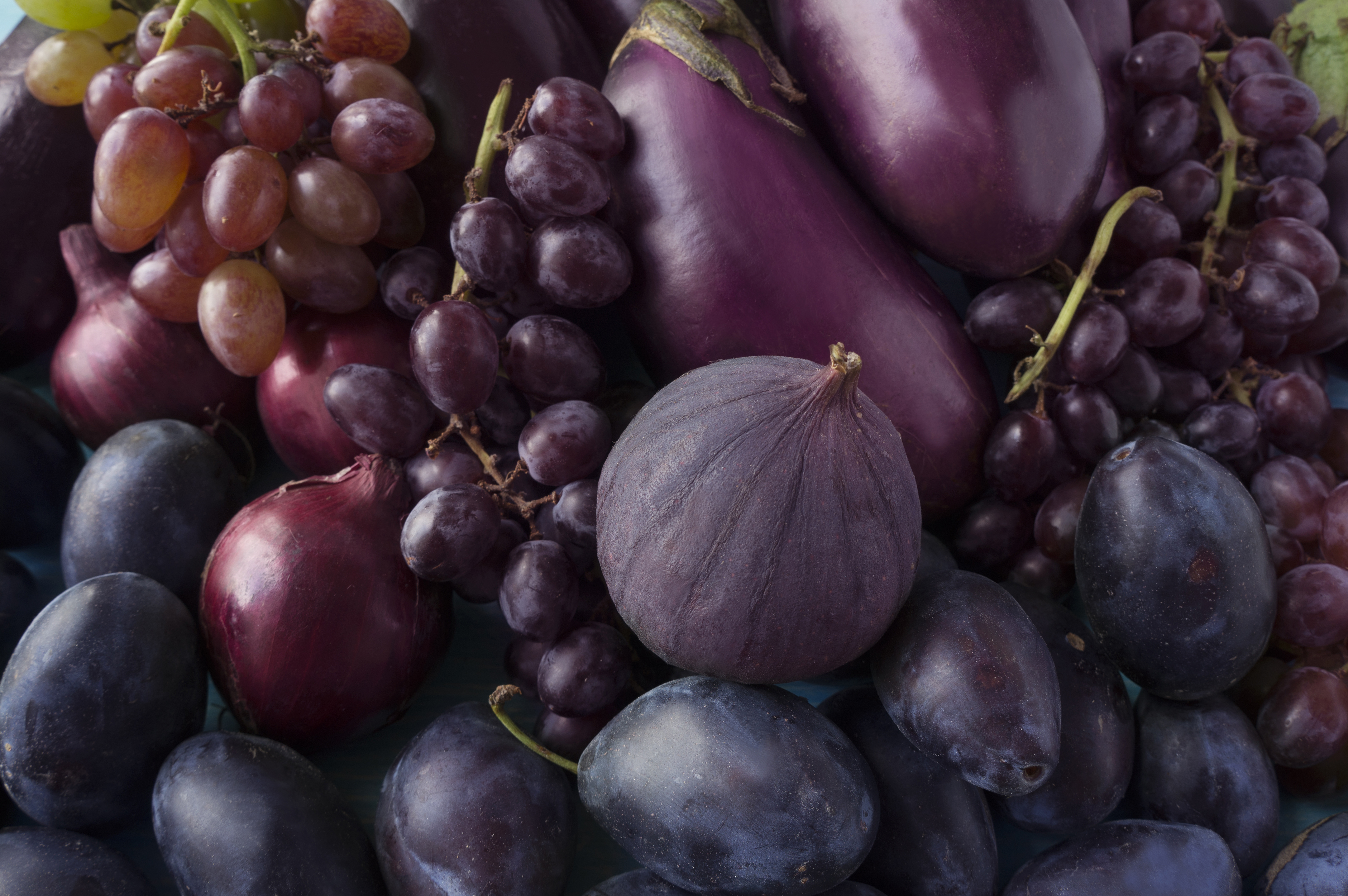 Pile of purple fruits and vegetables including grapes, plums, figs and eggplant