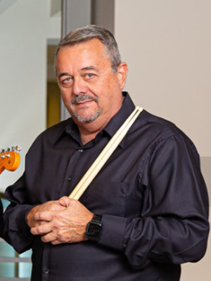 Ron Zalvo wears a black shirt while holding his drumsticks across his chest with both hands.