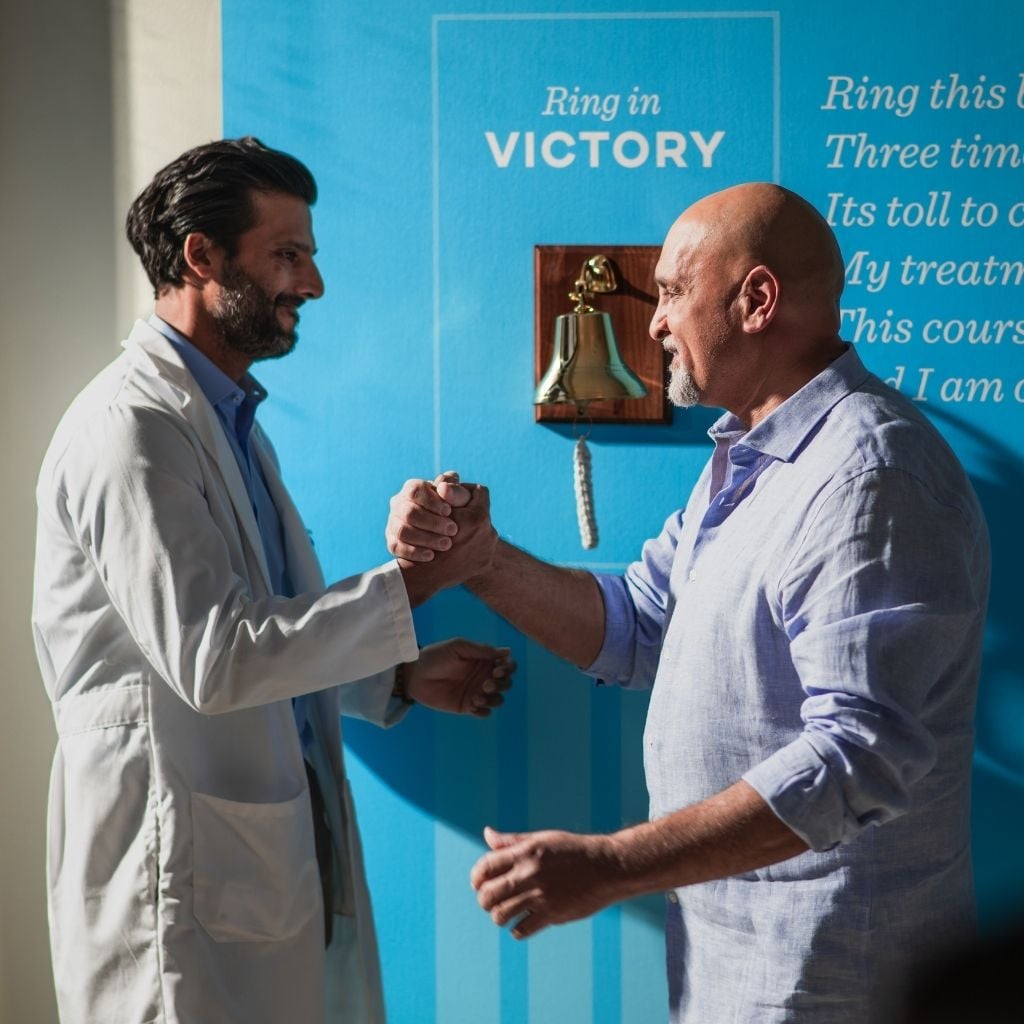 Doctor and patient embracing in front of cancer completion bell