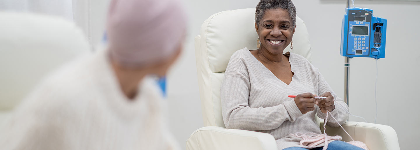 Two women chat while receiving intravenous chemotherapy. One woman is knitting.