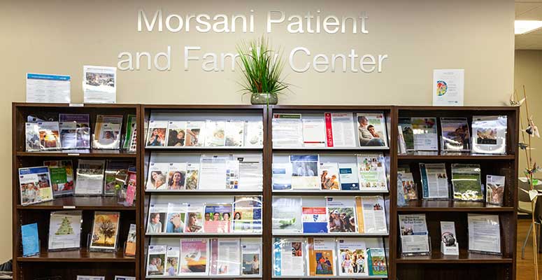 Bookshelves with cancer reading materials line the wall of the Morsani Patient and Family Center. There's a plant on the top of the bookshelves.