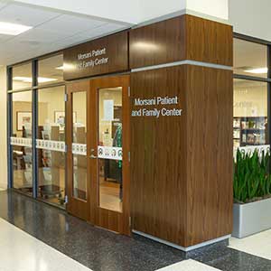 The exterior of the Patient and Family Center features wood walls, floor to ceiling glass windows and signage reading Morsani Patient and Family Center.