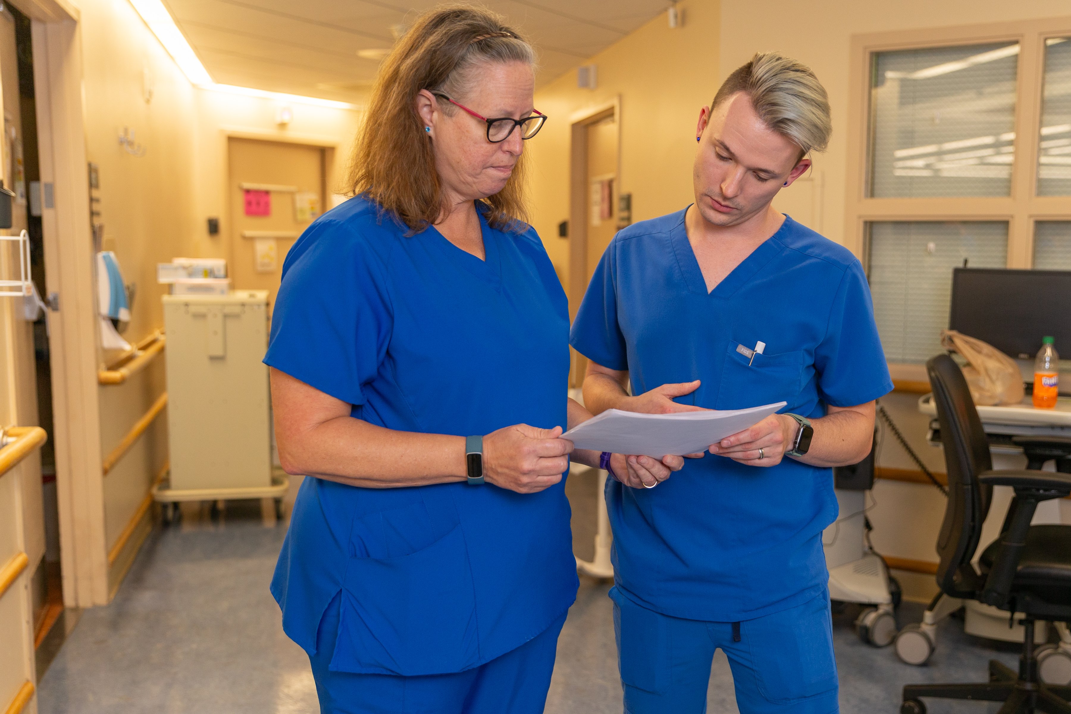 Two nurses in blue scrubs looking at records together