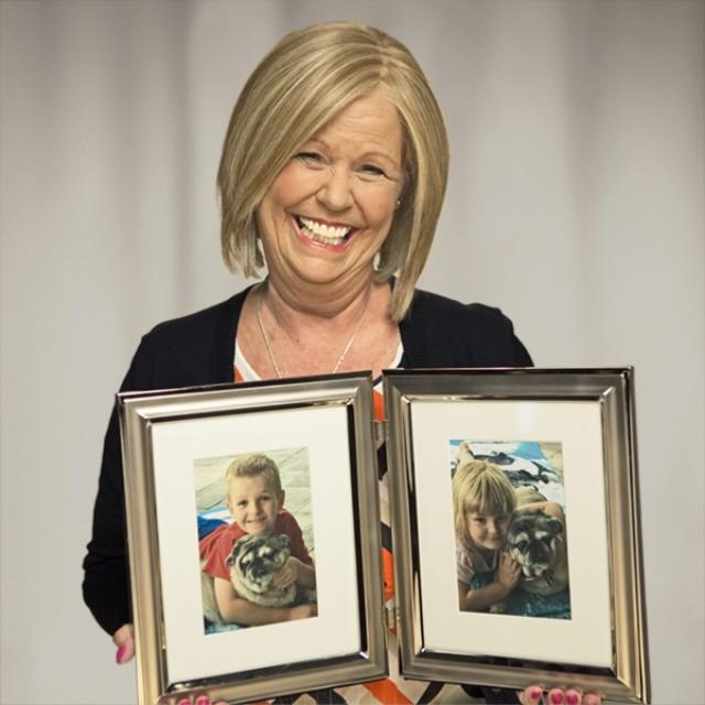 Ovarian cancer survivor, Donna, smiling and holding two framed pictures of her family and her dog. 