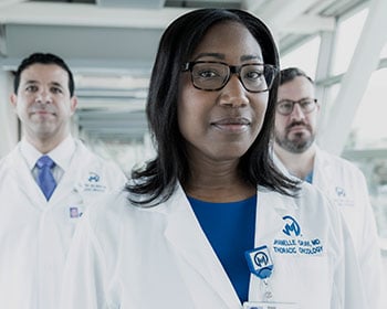 Physician stands in hallway with two doctors behind her. 
