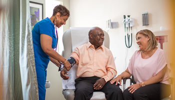 Man and woman sit with nurse checking his vitals.